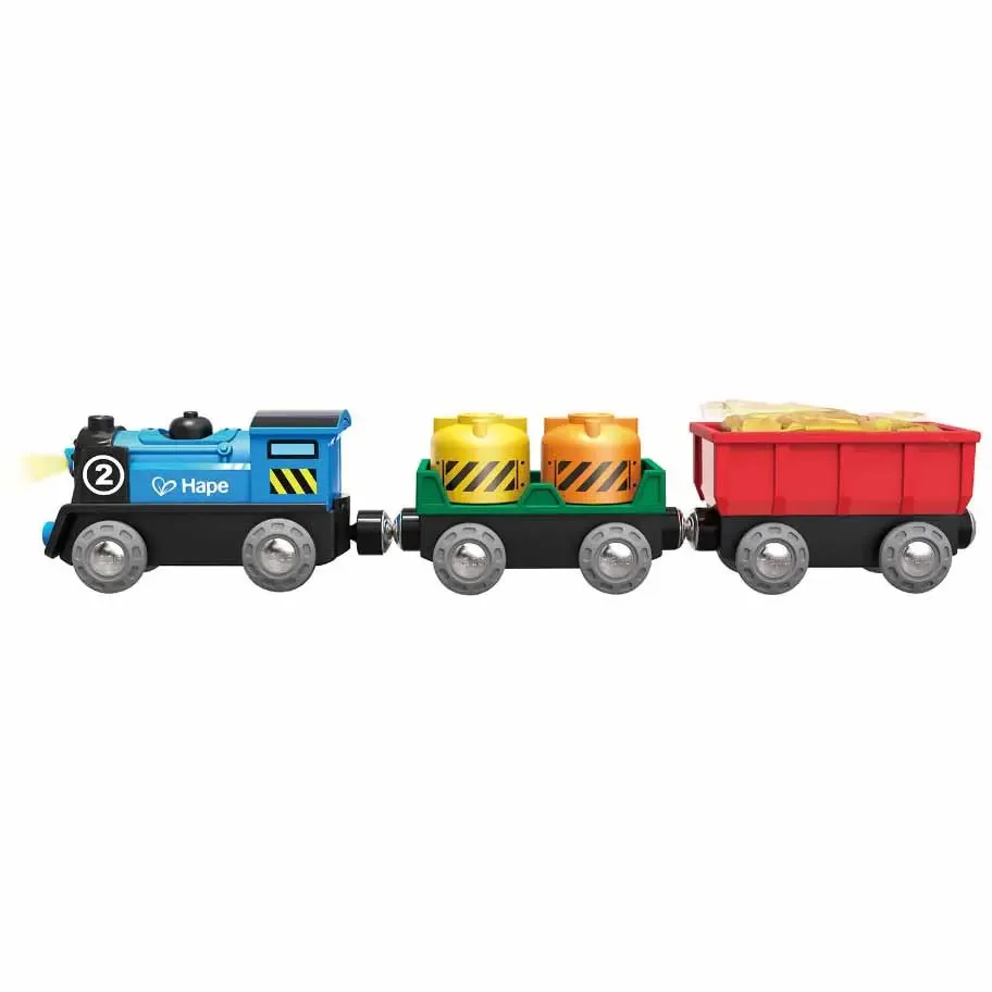 Blue toy locomotive with a front lamp pulling a green flat car with two canisters and a red open wagon, on a white background